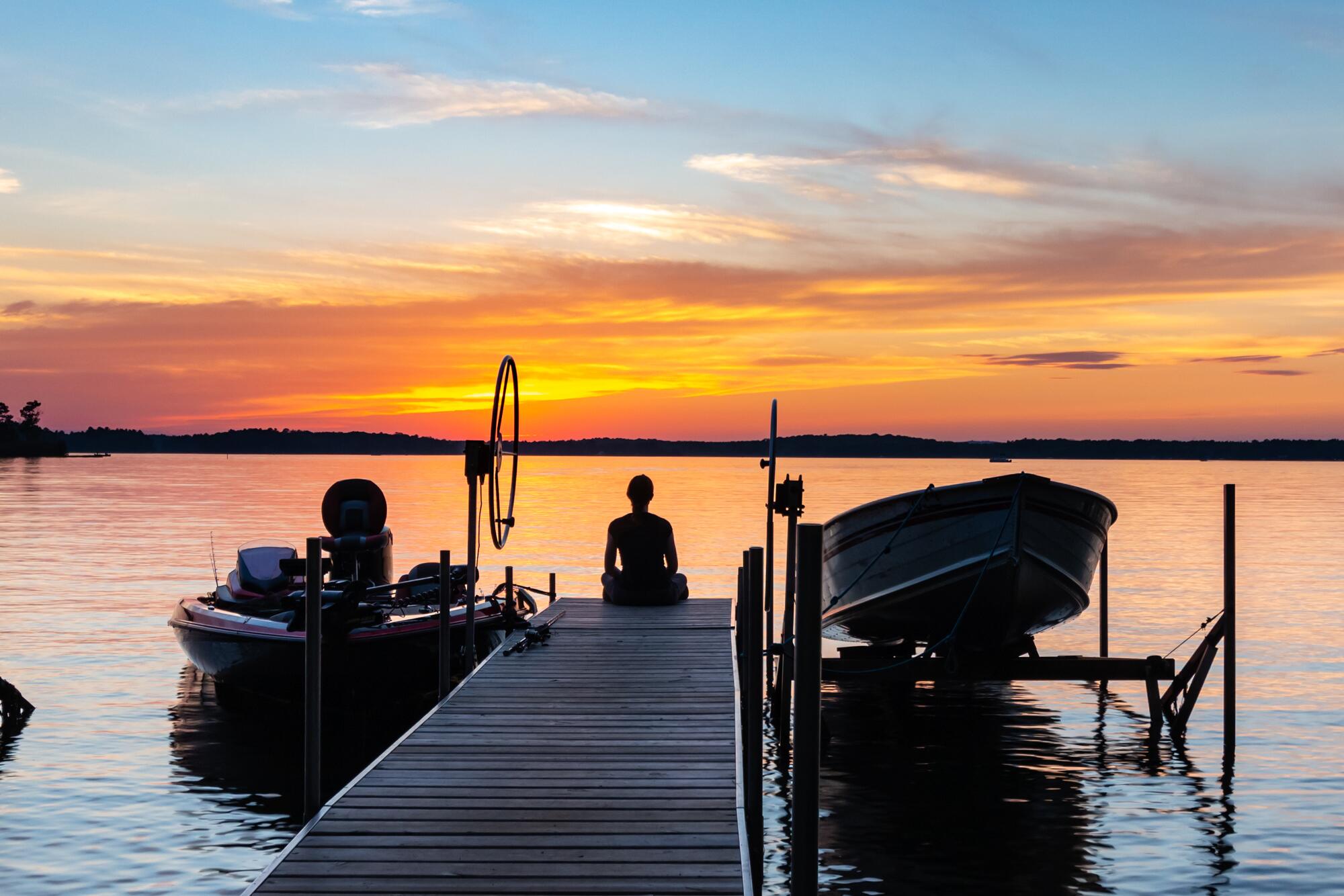 young_woman_sitting_on_the_end_of_a_pier_watching_the_colorful_sunrise